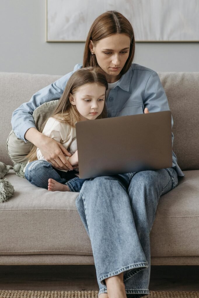 Mother and daughter sitting on sofa using laptop together, enjoying quality time indoors.